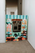 The Cozy Cube pretend play panel with ice cream shop and farmers market scenes