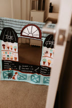 The Cozy Cube pretend play panel with ice cream shop and farmers market scenes