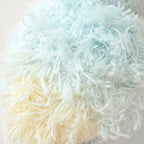 Close up of Cuddle+Kind baby parrot showing fluffy textured knit wings in pastel blue and yellow yarn