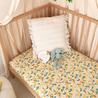 Sunny Citrus organic fitted cot sheet styled on a wooden nursery cot with neutral bedding creating a bright citrus themed baby room