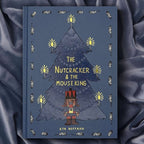 photoshoot of The Nutcracker & The Mouse King collector’s edition hardcover book with blue illustrated cover, gold foil title, festive Christmas design.