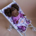 close up photo of baby doll kids stroller for pretend play with mini coletto doll inside. made by brand tiny harlow. print pictured is cherry gnigham