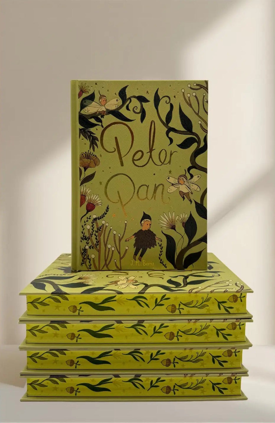 sprayed edges Peter Pan limited collector’s edition hardcover by J.M. Barrie with green illustrated cover, gold foil title, cloth-bound finish and decorative sprayed edges, stacked on books.