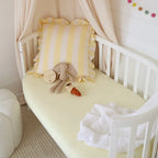 Snuggle Hunny Lemon Sorbet organic fitted cot sheet on a nursery cot styled with soft bedding and toys in a warm yellow tone