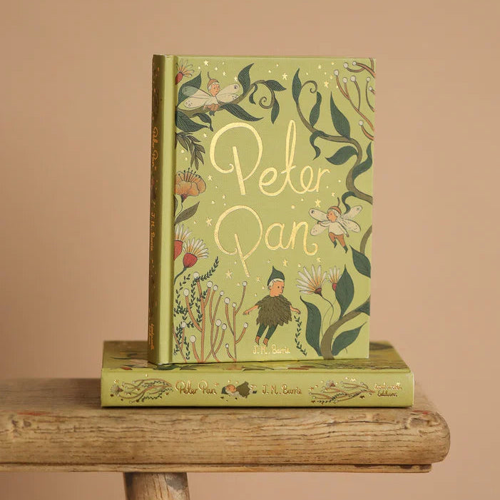 Peter Pan limited collector’s edition hardcover by J.M. Barrie with green illustrated cover, gold foil title, cloth-bound finish and decorative sprayed edges, stacked on books.