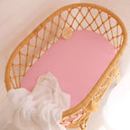 Snuggle Hunny Bubblegum organic bassinet sheet fitted on a woven bassinet with soft pink bedding in a cosy nursery setting