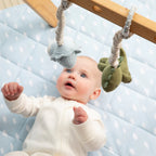 Baby playing under a wooden play gym with Living Textiles dinosaur hanging toys