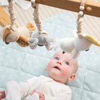 Baby playing under a wooden play gym with Living Textiles koala and cockatoo hanging toys