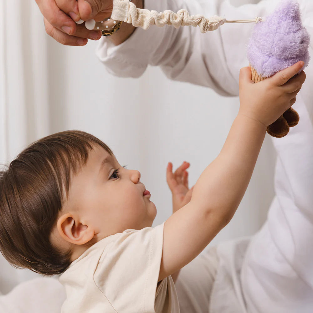 Baby reaching for Living Textiles ice cream and cupcake hanging stroller toys