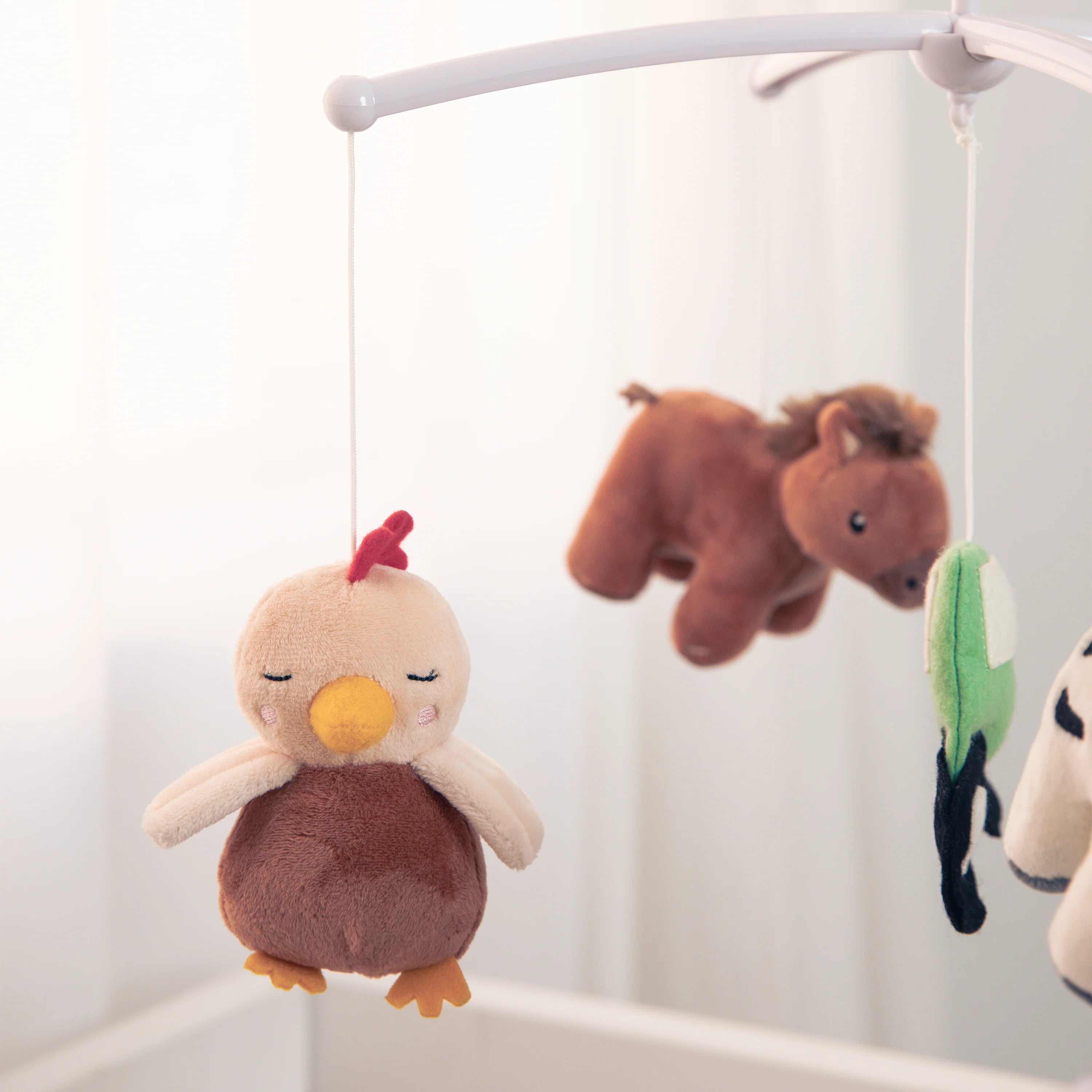 Plush animal toys hanging from a crib mobile with a neutral background