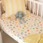 Beach Fun fitted cot sheet on baby cot mattress styled with yellow bedding showing snug stretch fit and soft breathable cotton