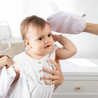 Baby in a white outfit with a white background and bath mitt