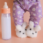 close up of the tiny tummies sleepytime pack gift set out of packaging, includes lilac daisy printed pyjamas for your doll, doll slippers, magic milk and play rattle for your doll and pretend play. brand is tiny harlow