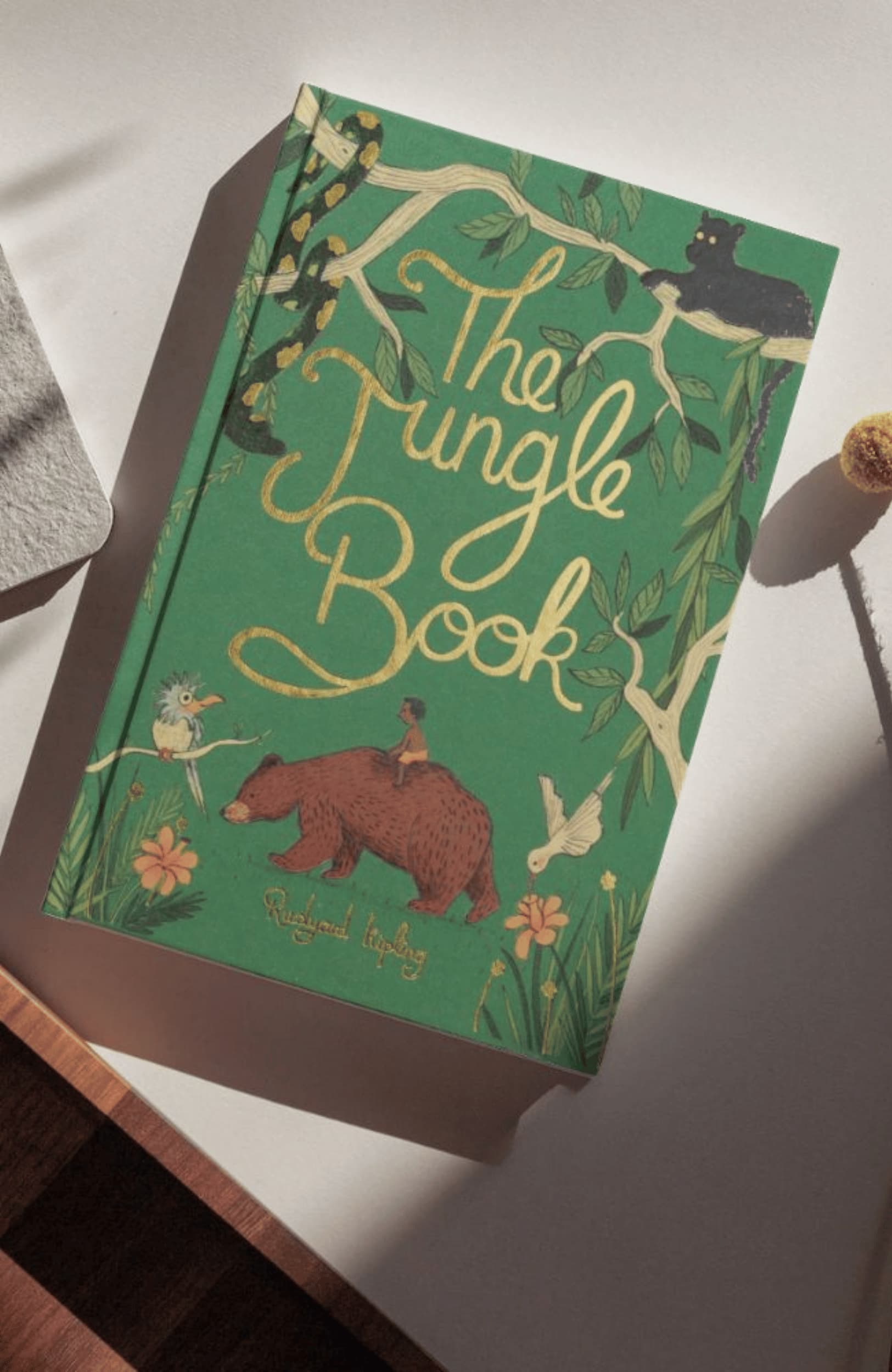photoshoot limited edition The Jungle Book collector’s edition hardcover by Rudyard Kipling with green illustrated cover, gold foil title, cloth-bound finish and decorative sprayed edges, stacked on books.