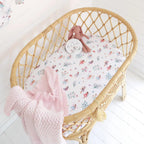 Fairy Garden organic bassinet sheet fitted on a woven bassinet in a cosy nursery with pink bedding and soft textures