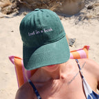 Person wearing a green cap with 'Lost in a book' text on a beach.