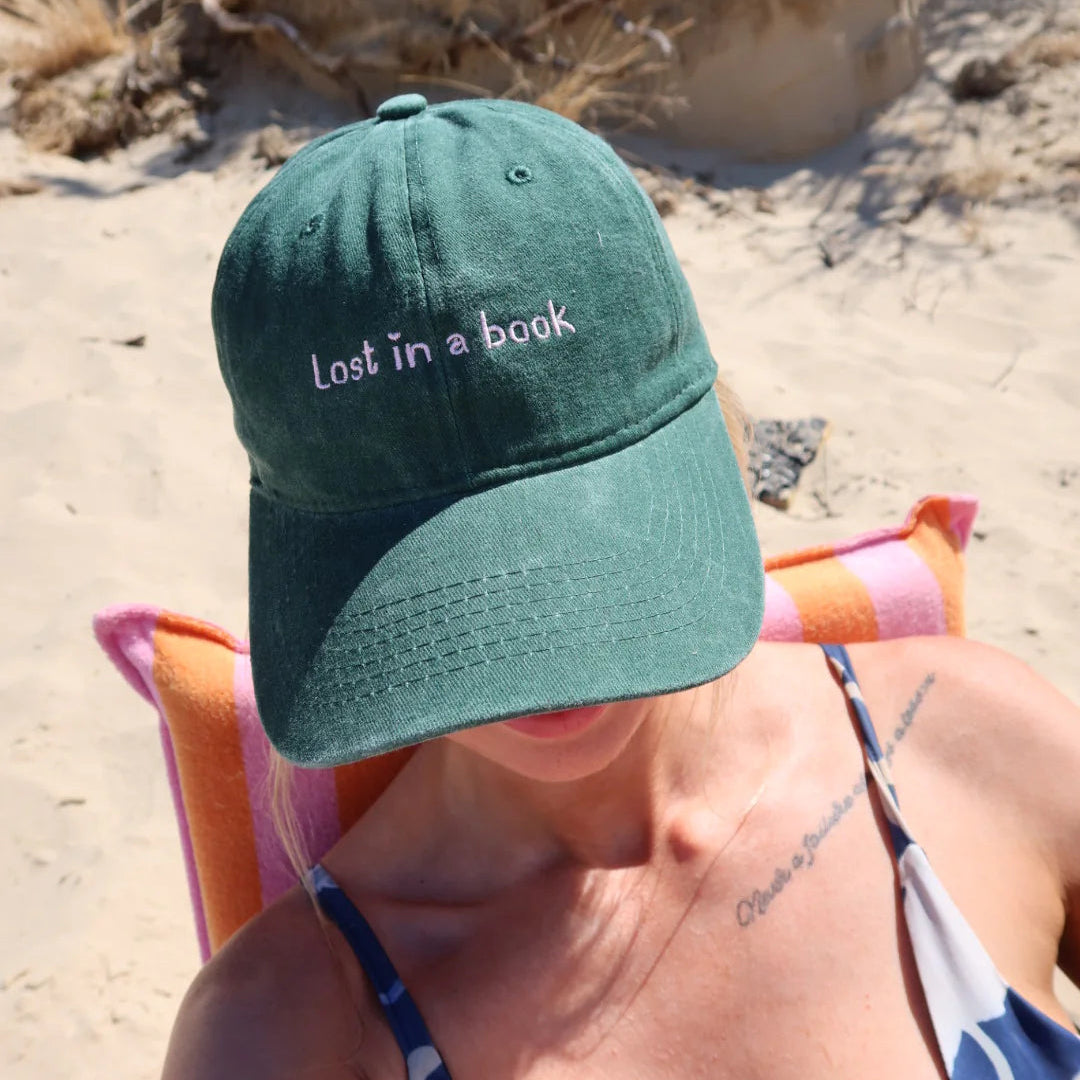 Person wearing a green cap with 'Lost in a book' text on a beach.