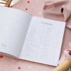 Open book with 'Contents' page on a pink surface with heart patterns