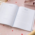 Open notebook with lined pages on a pink surface with heart patterns