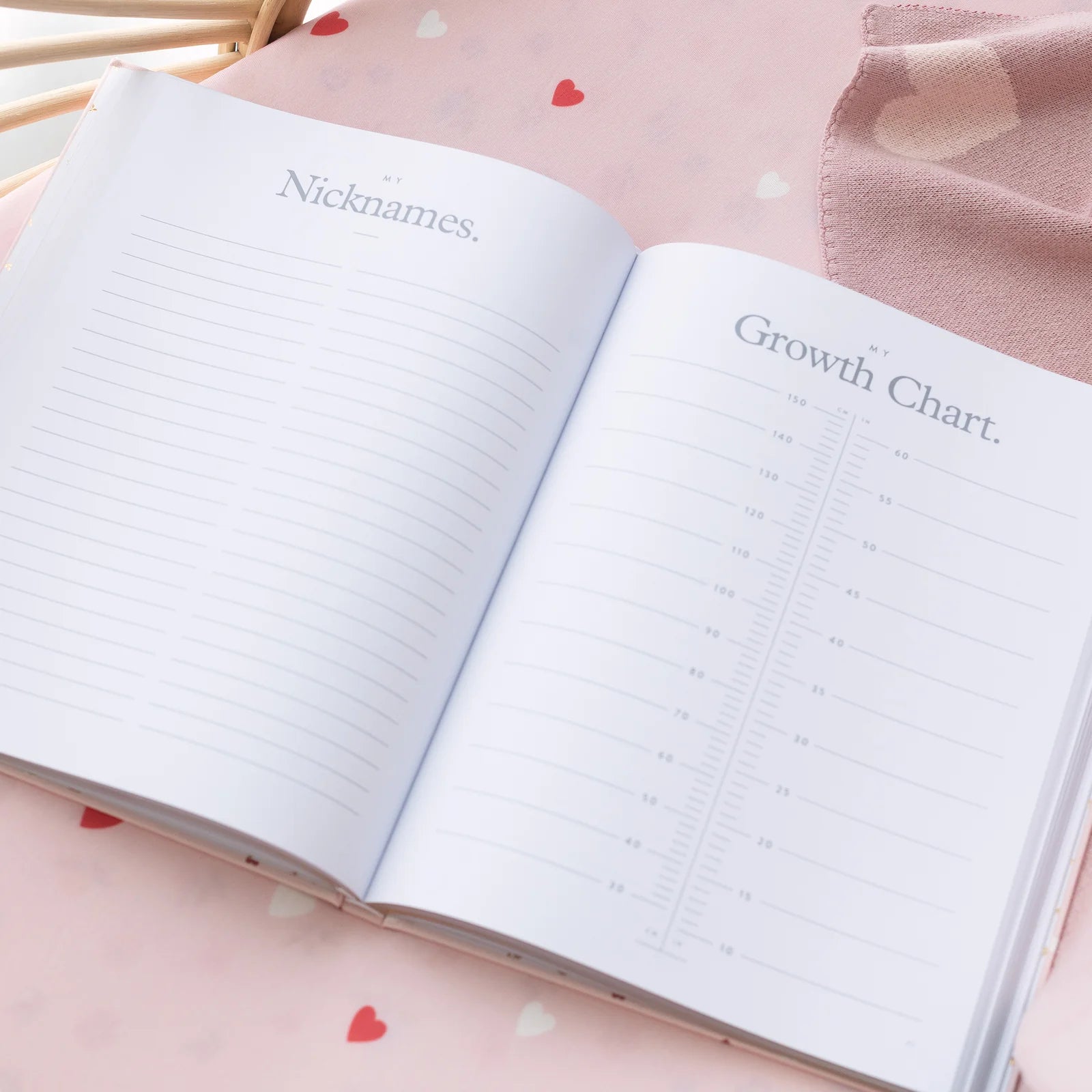 Open notebook with pages titled 'Nicknames' and 'Growth Chart' on a pink surface with heart patterns.