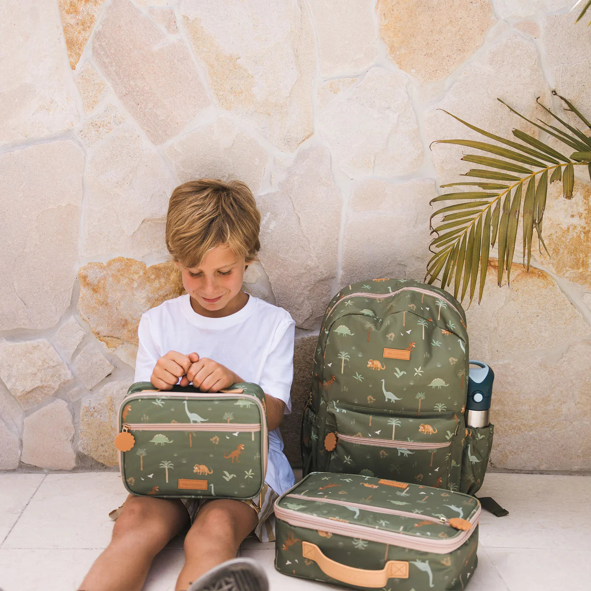 kid sitting with Fox & Fallow backpack for kids, perfect for school, daycare and everyday use. Spacious, practical and designed for little adventures. Personalisation of embroidery with name also available on bags in 2 placements. This print is dinos and has matching lunch bags