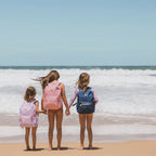 kids holding hands on beach wearing Fox & Fallow backpack for kids, perfect for school, daycare and everyday use. Spacious, practical and designed for little adventures. Personalisation of embroidery with name also available on bags in 2 placements. This print is forget me not, dusty roses and unicorns
