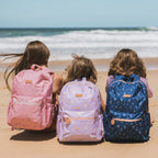 on beach photoshoot of Fox & Fallow backpack for kids, perfect for school, daycare and everyday use. Spacious, practical and designed for little adventures. Personalisation of embroidery with name also available on bags in 2 placements. This print is dusty roses, unicorns and forget me not