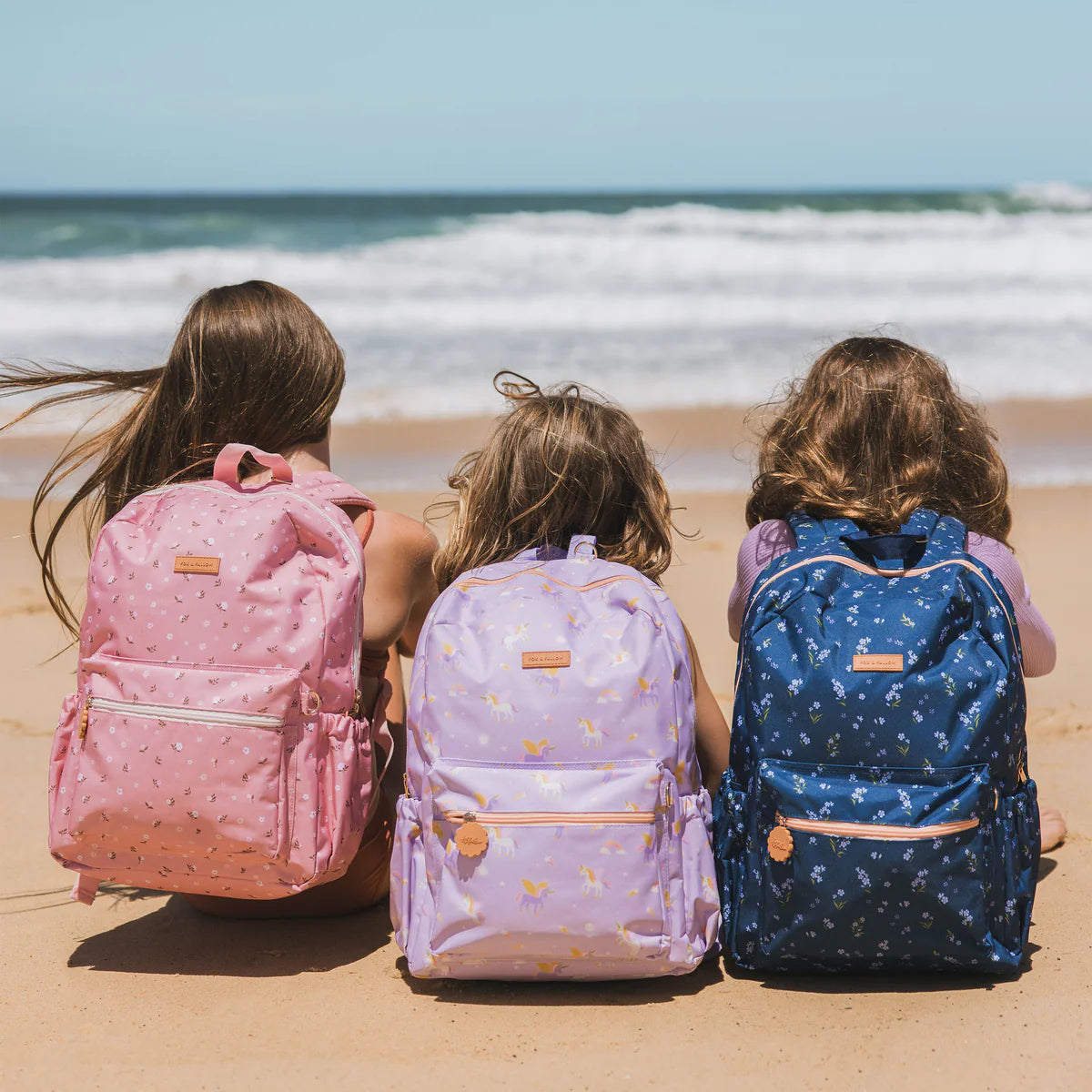 on beach photoshoot of Fox & Fallow backpack for kids, perfect for school, daycare and everyday use. Spacious, practical and designed for little adventures. Personalisation of embroidery with name also available on bags in 2 placements. This print is dusty roses, unicorns and forget me not