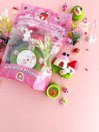 Kids sensory play kit with green strawberry scented dough, bunny village figurines, houses and textured mix-ins displayed beside packaging