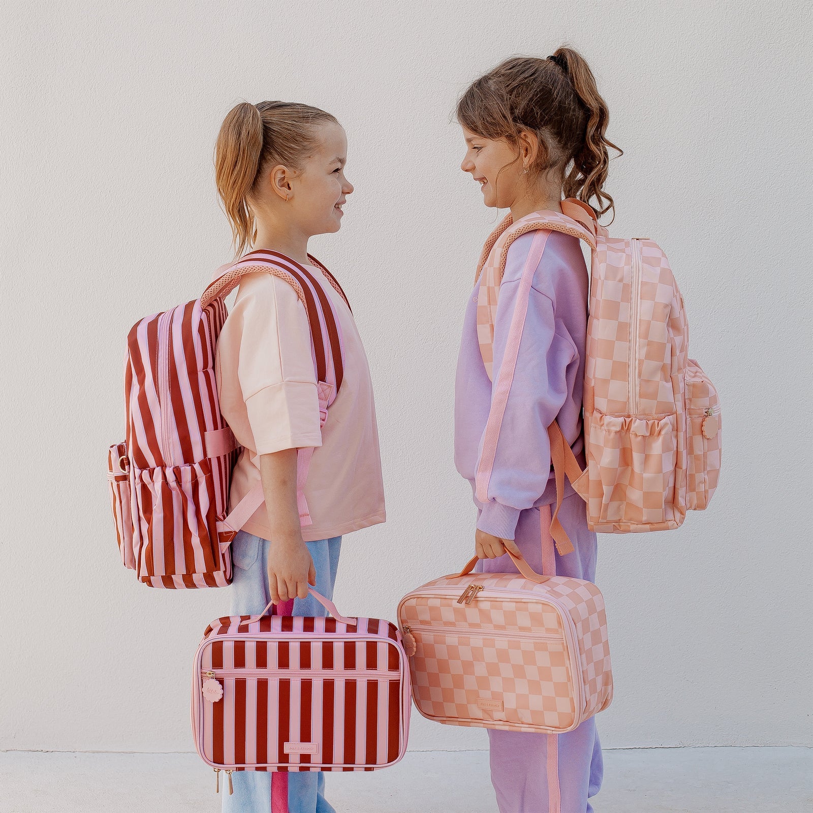children wearing Fox & Fallow backpack for kids, perfect for school, daycare and everyday use. Spacious, practical and designed for little adventures. Personalisation of embroidery with name also available on bags in 2 placements. This print is peach check and burgundy stripe with matching lunch bags