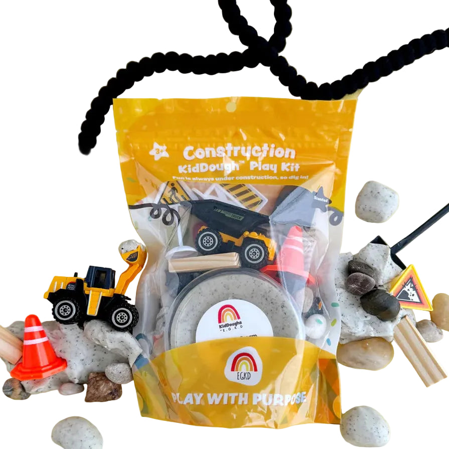 Construction themed sensory playdough kit with grey scented dough, toy trucks, safety cone, stones and building tools on a yellow background.