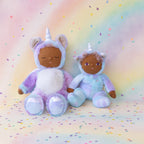 Two oli ella unicorn plush toys in unicorn costumes on a rainbow-colored background with polka dots.