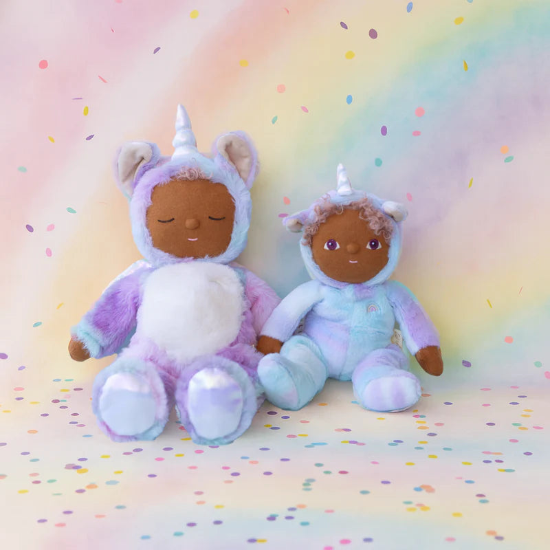 Two oli ella unicorn plush toys in unicorn costumes on a rainbow-colored background with polka dots.