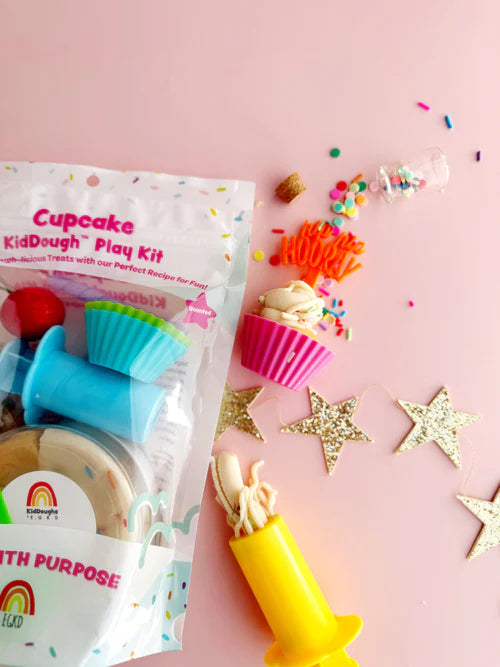Kids cupcake playdough baking set with pastel dough, sprinkles, cupcake moulds and decorating tools arranged on pink background for sensory and imaginative play