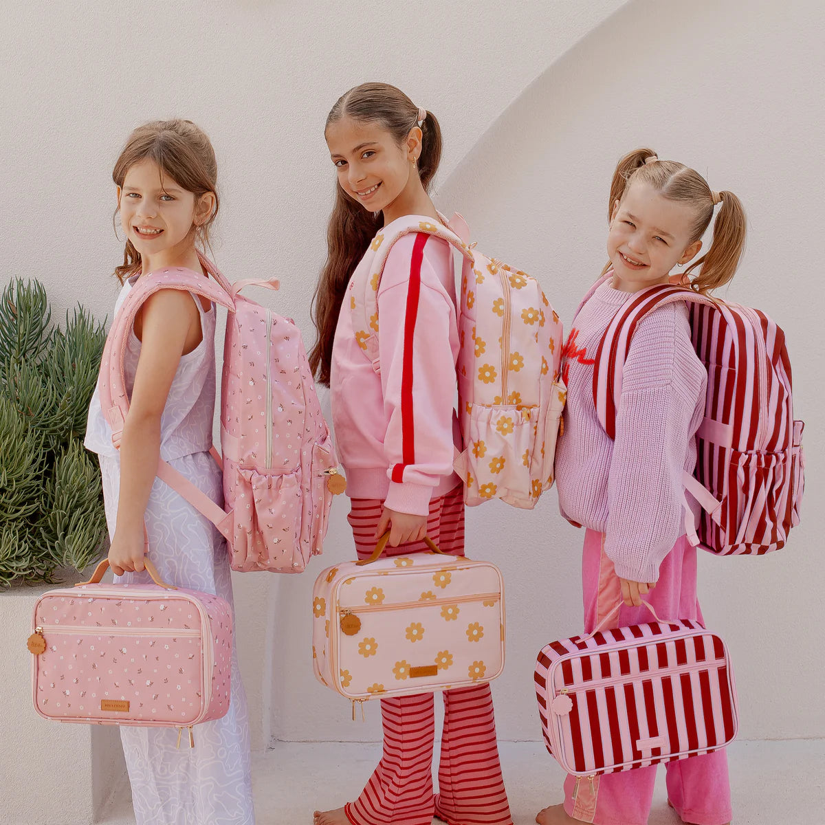 3 girls modelling Fox & Fallow backpack for kids, perfect for school, daycare and everyday use. Spacious, practical and designed for little adventures. Personalisation of embroidery with name also available on bags in 2 placements. This print is daisy chain, burgundy stripe and dusty roses