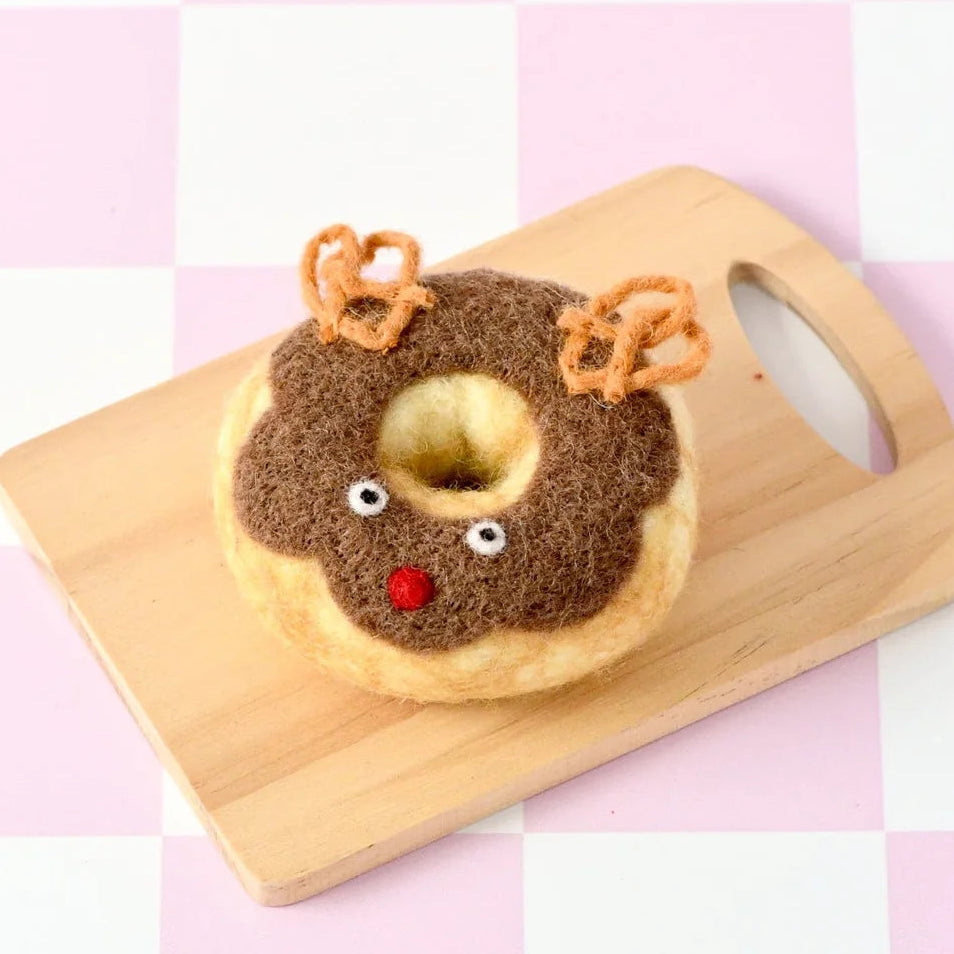 A novelty donut-shaped felt decoration shaped like a reindeer, displayed on a small wooden cutting board against a pink and white checkered background.