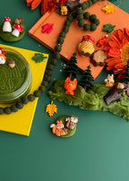 Woodland sensory play set with textured green playdough, forest animals, autumn leaves and tree pieces arranged for tactile pretend nature play