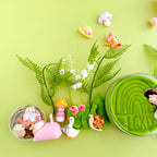 Garden sensory play accessories including green playdough, shovel, watering can, flowers and tiny garden charms arranged for tactile small world play