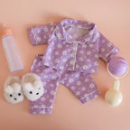 showcasing the tiny tummies sleepytime pack gift set out of packaging, includes lilac daisy printed pyjamas for your doll, doll slippers, magic milk and play rattle for your doll and pretend play. brand is tiny harlow