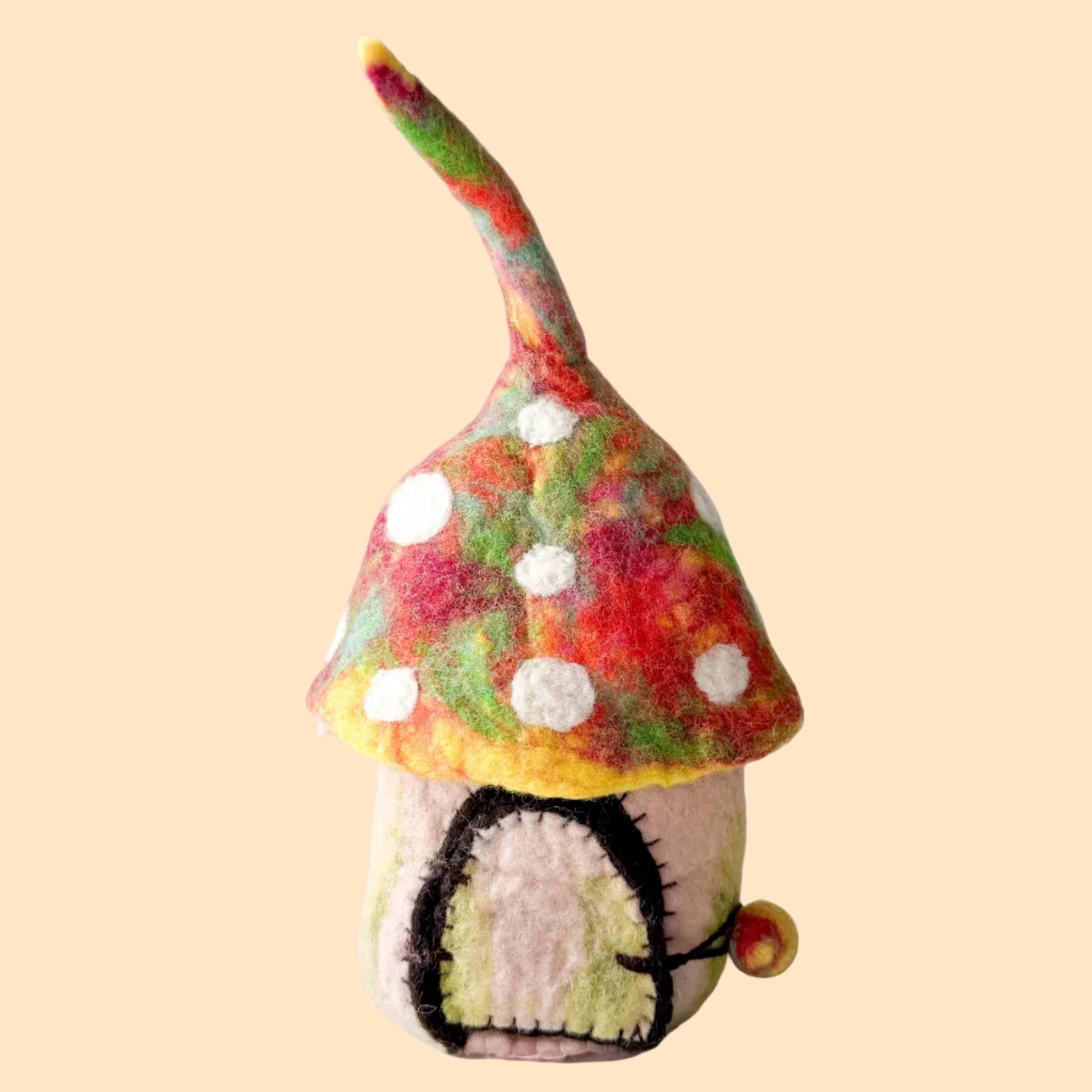 A handmade felt gnome figurine with a colorful mushroom-shaped hat, white polka dots, and a small pink body, standing on a textured white surface against a light gray background.