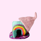 A small handmade felt house with a rainbow arch and a pink pointed roof, displayed on a white textured surface against a light gray background.