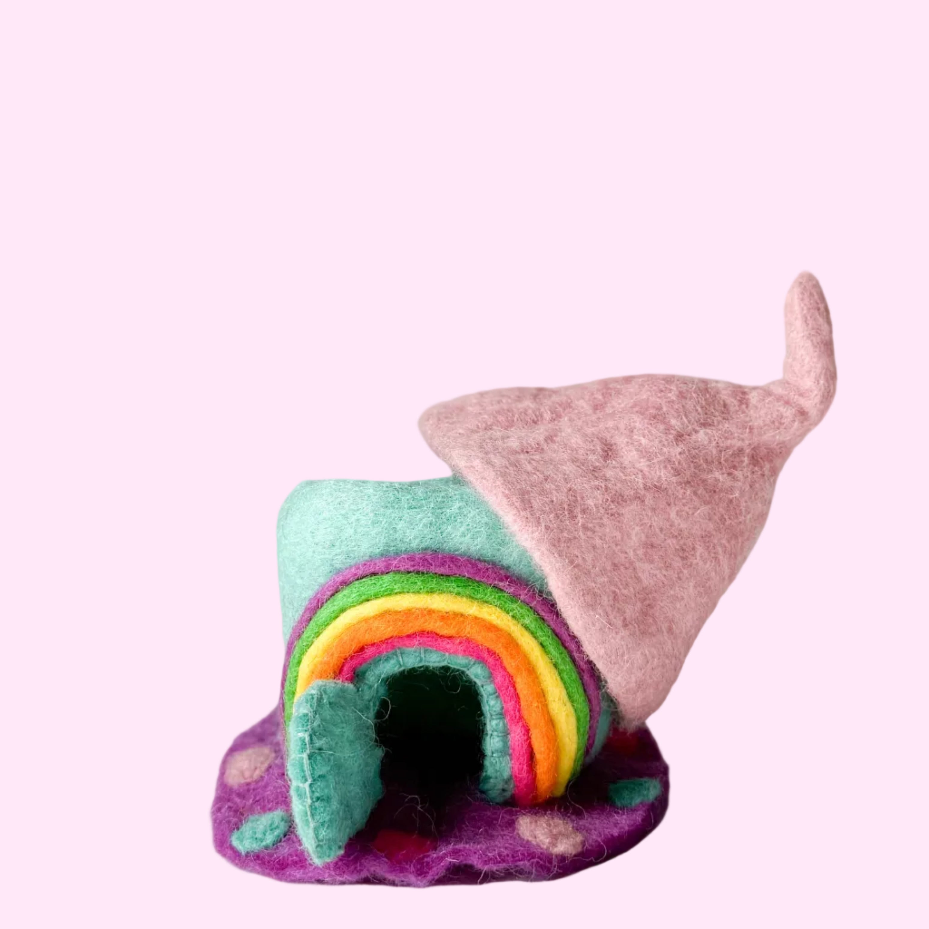 A small handmade felt house with a rainbow arch and a pink pointed roof, displayed on a white textured surface against a light gray background.