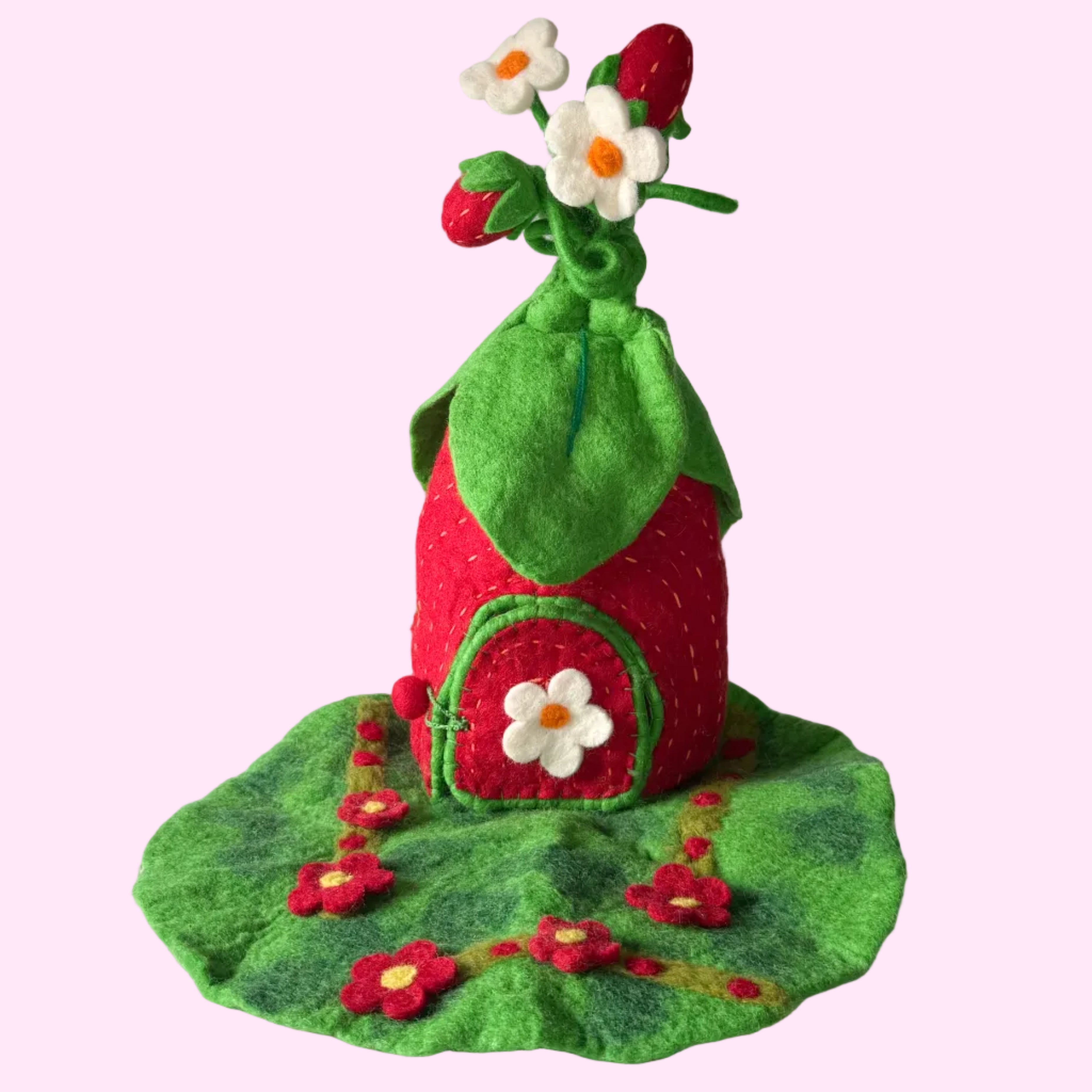 A handmade felt strawberry-shaped house decoration with a green leaf roof, red body, white flower on the door, and small white flowers on top, displayed on a textured white surface against a gray background.