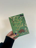 Hand holding a green book titled 'The Jungle Book' with illustrations on a white background