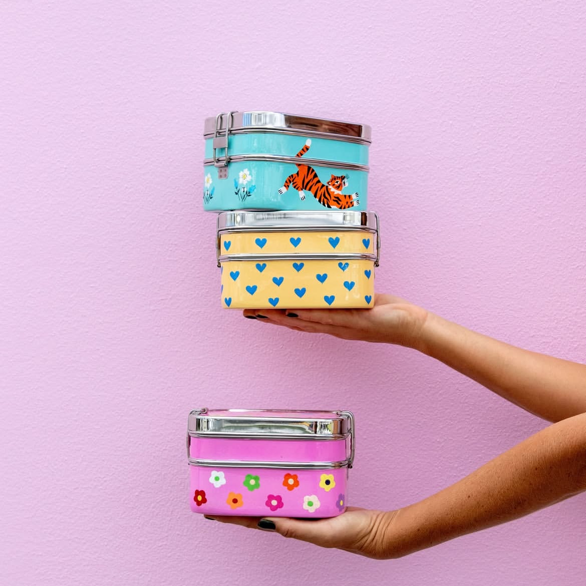Three-tiered nesting lunch box set held by a hand on a pink background, with 'picnicfolk' branding.