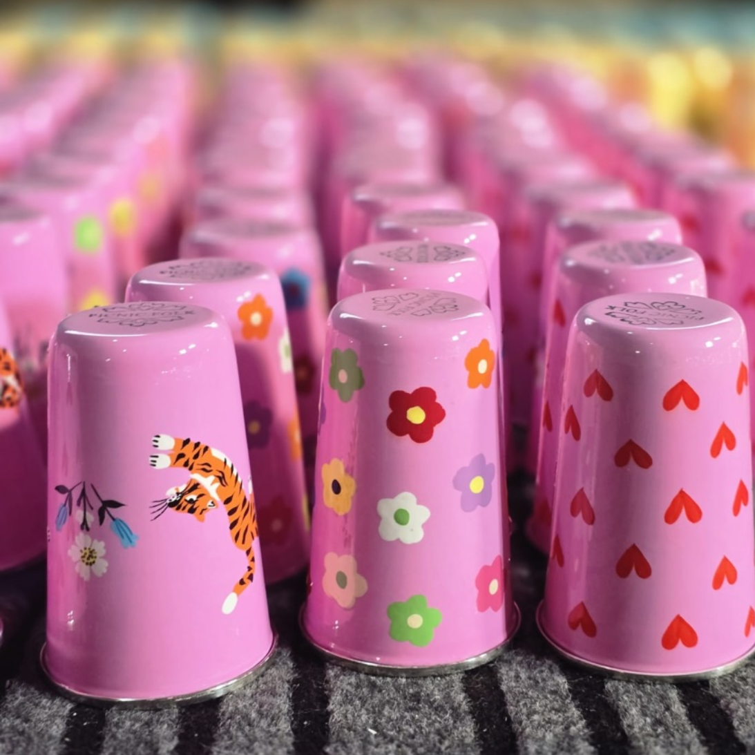 Pink cups with various designs on a textured surface, from a Picnic Folk product line