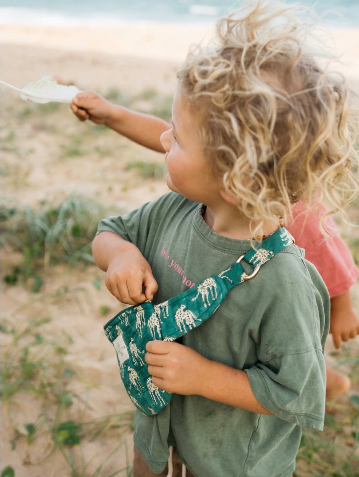 Child holding a green bag with animal prints outdoors at beach with crossbody bag for adventure collecting