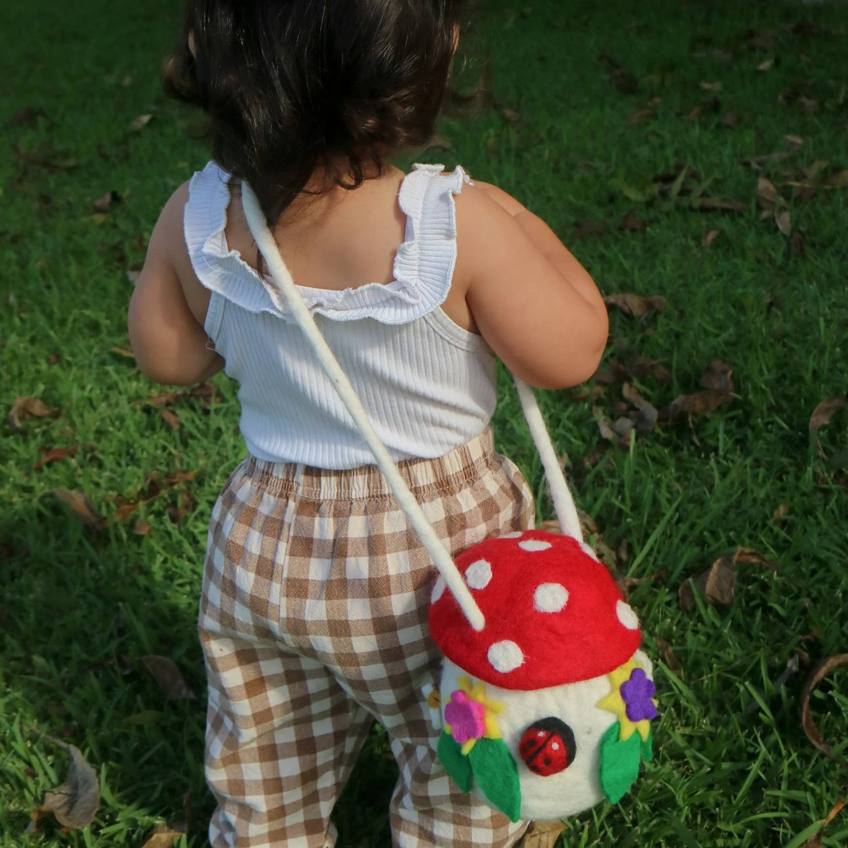 Child wearing the handmade Hey Junii Mushroom Forager Bag with wool felt mushroom design, floral details, ladybug and adjustable shoulder strap.