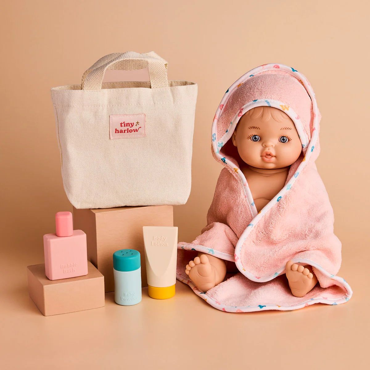 photoshoot of the tiny harlow bath accessory pack that comes with a bag, body lotion,baby doll towel, baby powder and bubble bath all for pretend play with dolls called tiny bath time
