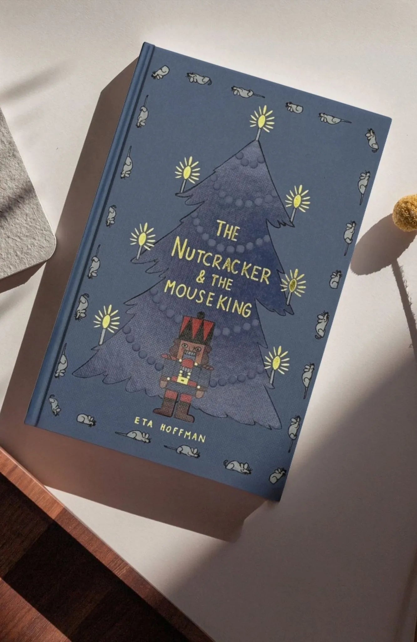 photoshoot in sun of The Nutcracker & The Mouse King collector’s edition hardcover book with blue illustrated cover, gold foil title, festive Christmas design.